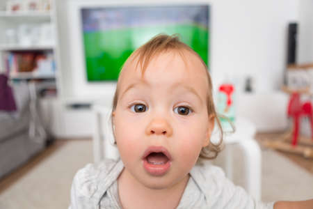 One and a half year old toddler girl looking at the camera with her eyes wide open; wide angle shotの写真素材