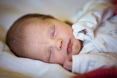 Newborn baby girl sleeping in her crib, lit by the morning sun; stork bites visible on forehead and eyelidsの写真素材