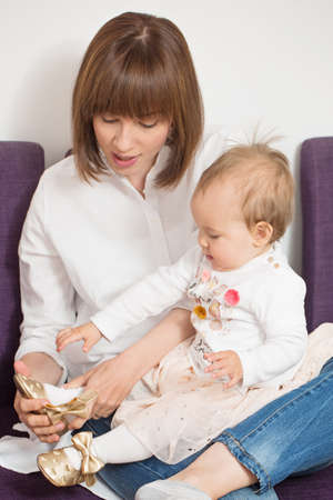 Mother holding an one year old baby daughter and helping her put the shoes onの写真素材