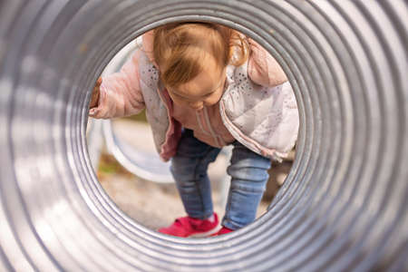 One and a half year old baby gir holding playing by the end of the metalic tunnel, entering on one sideの写真素材