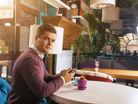 Young man holding a mobile phone and smiling. Read the posts and drinking coffee.の写真素材