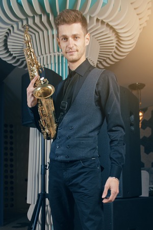 A young man in a suit standing with a saxophone musical instrumentの写真素材