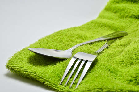 Spoon and fork wrapped in a napkin green on white backgroundの写真素材