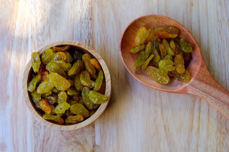 raisins in a wooden bowl with spoon on wood table backgroundの写真素材