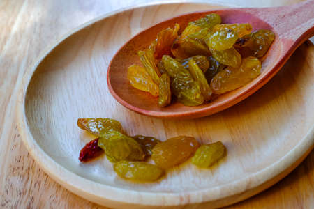 raisins in a wooden bowl with spoon on wood table backgroundの写真素材