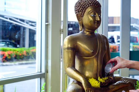 A Buddhist extending an arm to pour water over a Buddha statue, a traditional cleaning given during the Thai new year of Songkranの写真素材