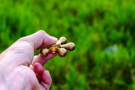 closeup of a young caucasian man playing with a brass fidget spinner, on nature background