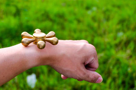 closeup of a young caucasian man playing with a brass fidget spinner, on nature backgroundの写真素材