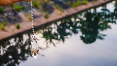 Men hand holding and using quartz crystal pendulum and using it, nature background.の写真素材