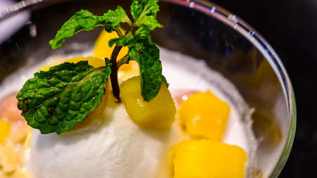 Frozen yellow mango sorbet, berry ice cream in a mask with mint and blueberries. Gray background....