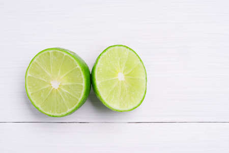 Natural fresh lime and sliced, green leaf isolated on white wooden background.