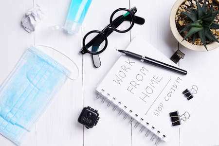 Flat lay, top view office white table wooden desk. Workspace with blank eyeglasses, diary, mask, and...