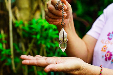 Foretelling the future with crystal pendulum. holding and using quartz crystal pendulum and using it, nature background.の写真素材