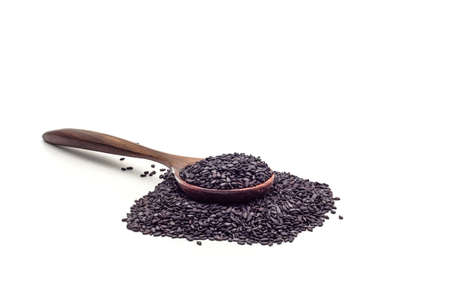 Pile of scattered black sesame seeds with a wooden spoon isolated on white background. Scientific...
