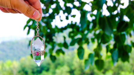 Men hand holding and using quartz crystal pendulum and using it, nature background.の写真素材