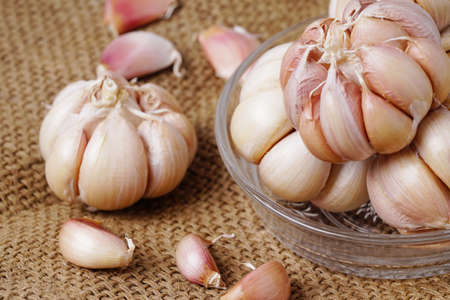 Garlic Cloves and Bulb in glass bowl on hemp sack. Garlic bulbs on rustic old table. Fresh gralic...