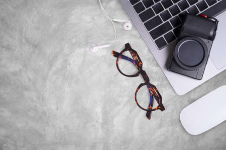 Flat lay gray concrete table office desk top with computer and camera, eye glasses, mouse and supplies. Top view with copy space.の写真素材