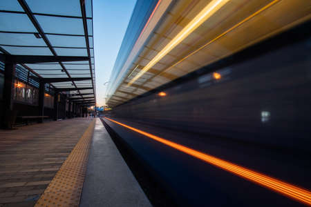 Empty platform of tramway station with motion blurred tram. Platform of light rail system at dusk.