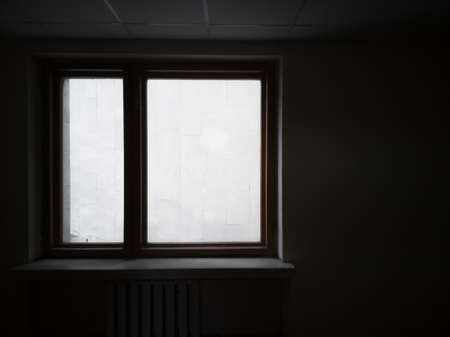 Window overlooking the wall. Silhouette of a window in dark interrior behind which the wall is...