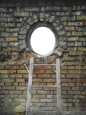 Frame in the shape of a circle window lined with old, aged damaged yellow bricks with a metal ladder...