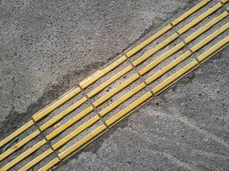 Abandoned dirty yellow tactile tiles is laid on the asphalt, top view.