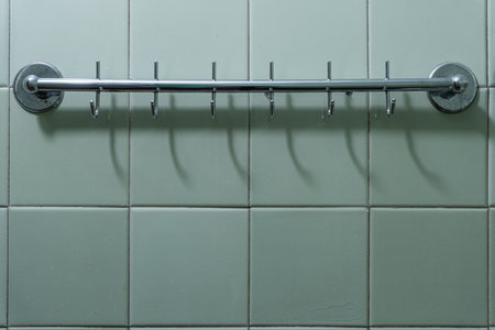 Textured empty obsolete metal hanger on the wall is lined with glossy ceramic tiles in the bathroom...