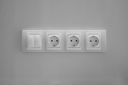 Three plastic sockets with a double switch on a gray wall. Textured.