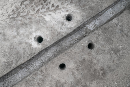 A trench in the pavement in concrete for a cable and 4 holes for anchor bolts, top view.