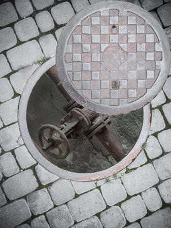 An old rusty pipe at the bottom of an open sewer manhole on the sidewalk.の写真素材