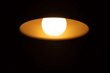 Warm orange LED lamp in the ceiling on a dark background in the center of the frame, bottom view.