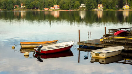 Small row boats tied to a pier with parked canoes on top  In the background some Swedish houses are visible by the shore の写真素材