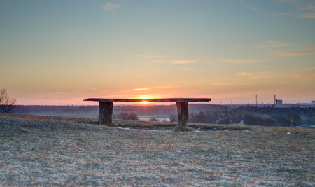 Bench overlooking an early spring landscape with the sun rising on the horizonの写真素材