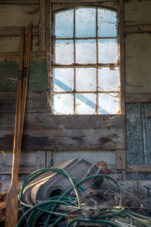 By a window in an old and worn building a mess lyes beneath and a pair of oars beside it の写真素材