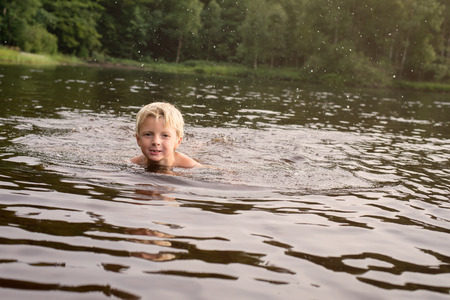 Young boy swimming in a lake late afternoon with water splashing around him の写真素材