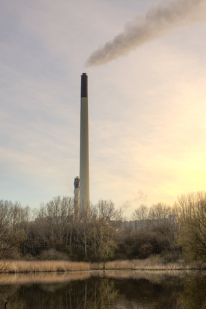 A huge chimney on a power plant is illuminated by the morning sunの写真素材