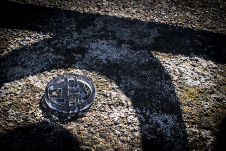 Clear dark plastic bit coin on a stone formation with shadows of fence.の写真素材