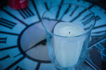 Clock table with turned off white candle and glass cup, elapsed time symbol.の写真素材