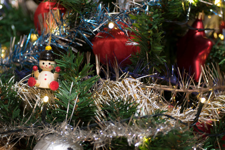 Artificial christmas tree decorated with wooden figurine, decoration for christmas tree, lights, tinsel and garland, red ballsの写真素材