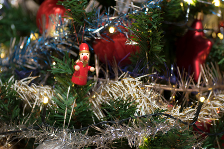 Artificial christmas tree decorated with wooden figurine, decoration for christmas tree, lights, tinsel and garland, red ballsの写真素材