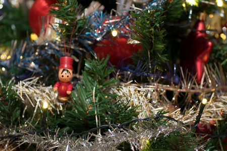 Artificial christmas tree decorated with wooden figurine, decoration for christmas tree, lights, tinsel and garland, red ballsの写真素材