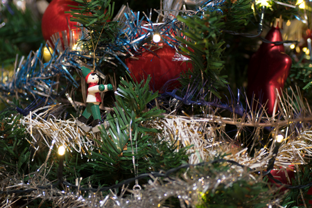 Artificial christmas tree decorated with wooden figurine, decoration for christmas tree, lights, tinsel and garland, red ballsの写真素材