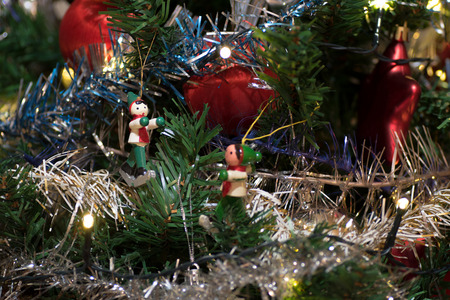 Artificial christmas tree decorated with wooden figurine, decoration for christmas tree, lights, tinsel and garland, red ballsの写真素材