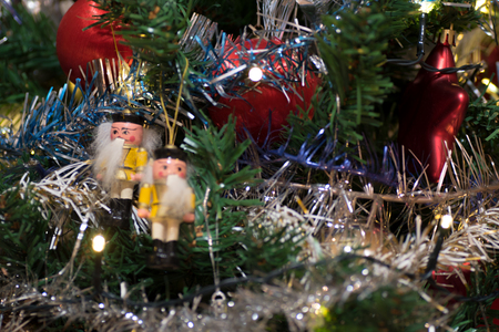 Artificial christmas tree decorated with wooden figurine, decoration for christmas tree, lights, tinsel and garland, red ballsの写真素材