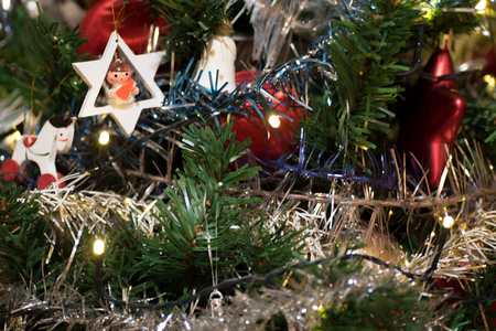 Artificial christmas tree decorated with wooden figurine, decoration for christmas tree, lights, tinsel and garland, red ballsの写真素材