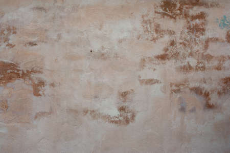 An old wall with a bright faded orange color and a bit of fallen plaster and peeling paint.の写真素材