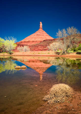 Unusual spire-like rock formation casting a reflection on a calm Utah pondの写真素材