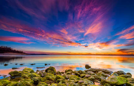 Amazing multicolored sunset over Benbrook Lake in Fort worth, TX featuring vivid green mossy rocks in the foregroundの写真素材