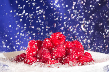 Plate full of fresh raspberries under falling water dropsの写真素材