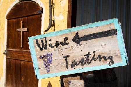 Weathered, handpainted wine tasting sign in front of an old adobe buildingの写真素材