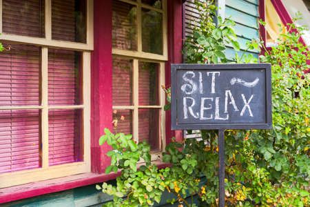 Hand-made chalkboard sign in front of a colorful gallery imploring visitors to "sit and relax"の写真素材